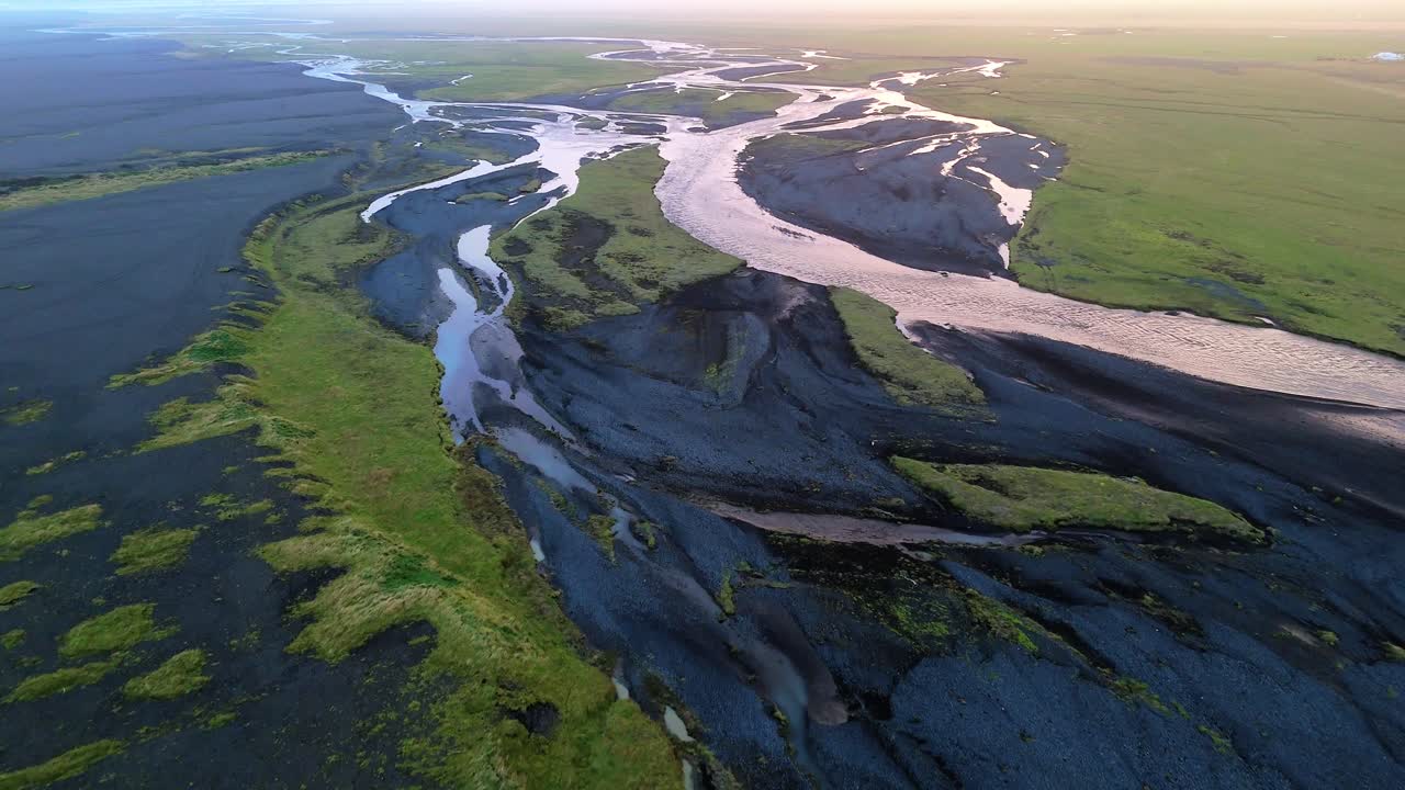 Icelandic streams twist like veins on their journey through glaciated valleys, volcanic rock and vibrant mossy green flatlands to the sea. Drone aerial fly over dramatic landscape