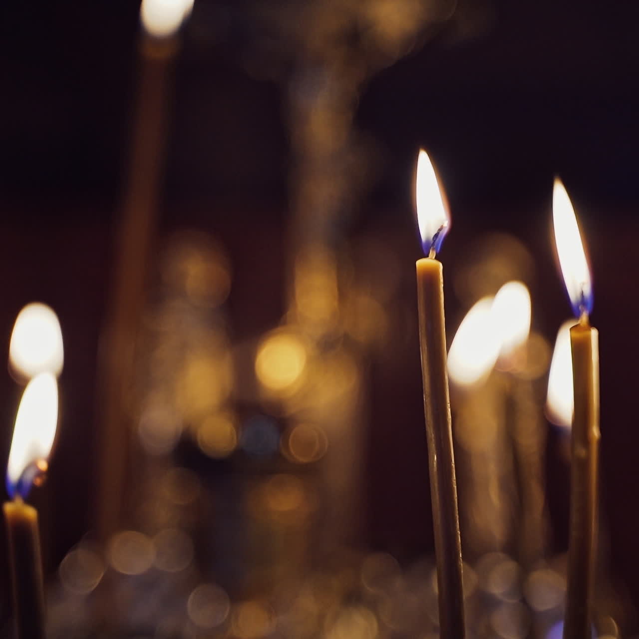 Many candles burning in the night temple. Abstract candles background. Yellow candle flames glowing on blur dark background in church.