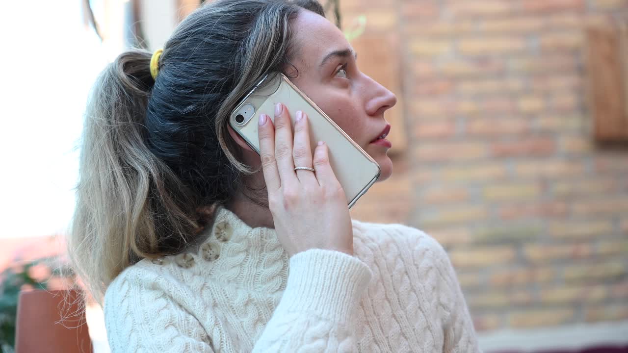 Close up of a woman in a white turtleneck talking on her phone in a restaurant