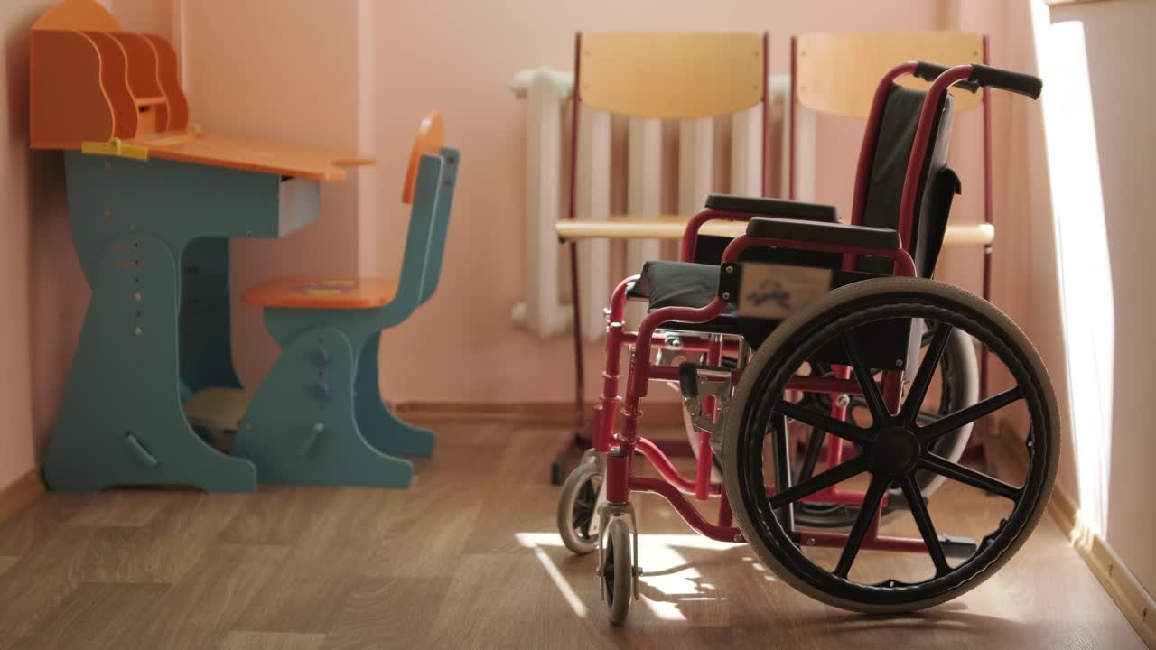 una silla de ruedas infantil está de pie en el medio del pasillo de la escuela contra el fondo de un escritorio escolar. centro de rehabilitación para niños.