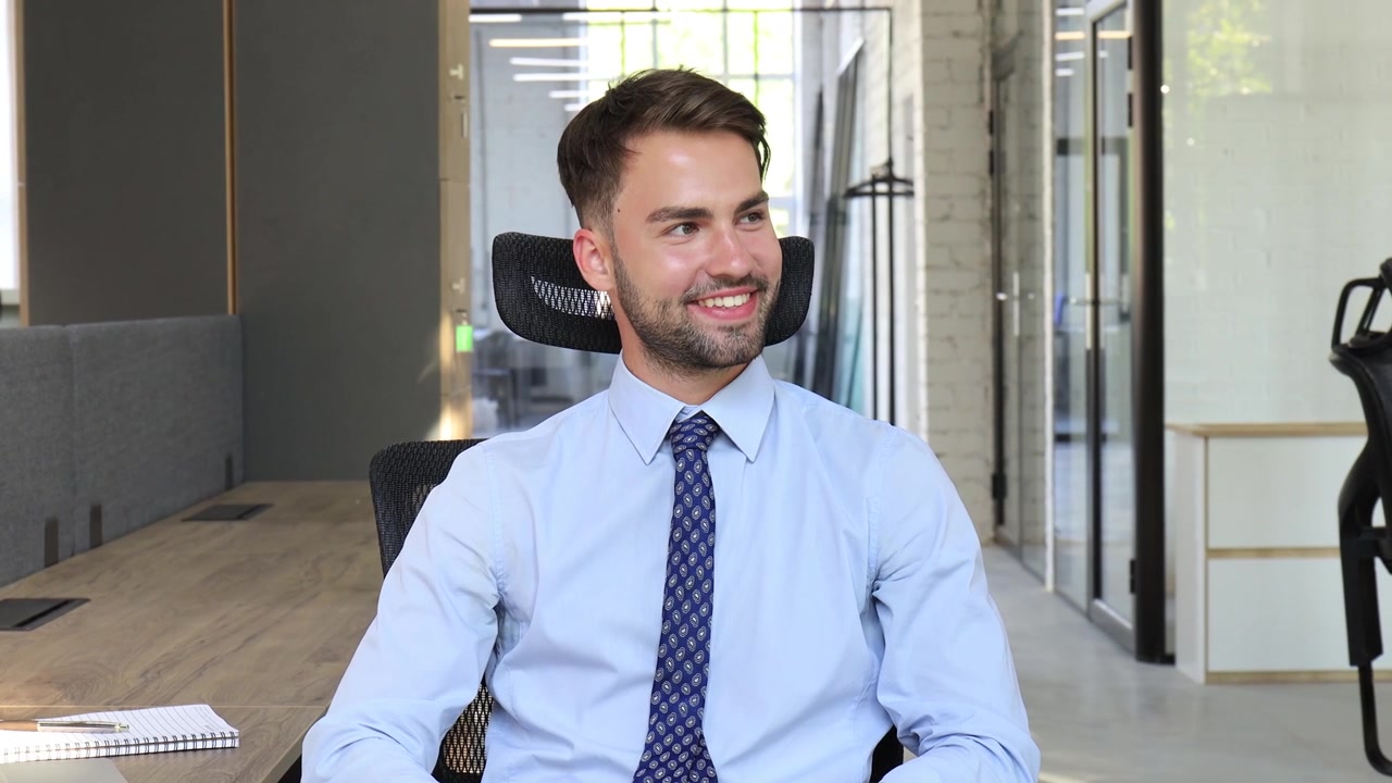 Jovem Empresário Sentado na Cadeira do Escritório, Olhando para Longe e Sorrindo