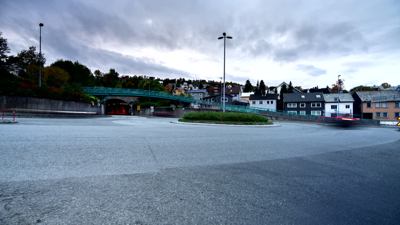 노르웨이 트롬소 (tromso) 의 구름이 가득한 해가 지는 동네를 가로지르는 아스팔트 도로의 교통.