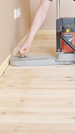 sanding wooden floor edges with a sanding machine, close-up, focusing on the hand