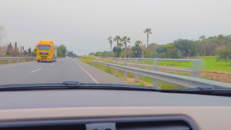 A-fast-drive-view-from-the-windscreen-of-a-car-making-amaze-of-travel-on-the-highway-of-Mallorca,-Spain,-with-lush-greenery-in-rainy-weather,-light-and-heavy-traffic-passing-from-the-other-side