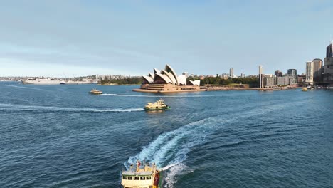 Impresionante-Toma-Aérea-De-Aproximación-De-La-Emblemática-ópera-Australiana-De-Sydney-Con-Ferries-De-Pasajeros-Debajo,-Australia