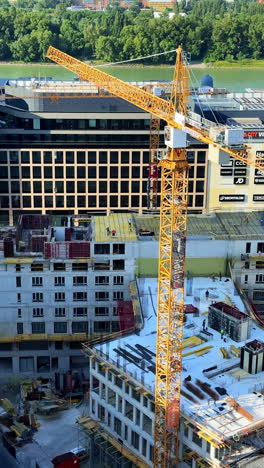 cranes by river construction. a crane lifts materials at a construction site by a river with buildings in the background during the day
