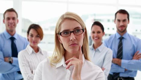 Mujer-De-Negocios-Mirando-A-La-Cámara-Con-Colegas-Detrás-De-Ella