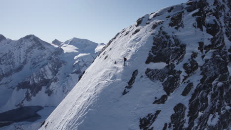 Vista-Aérea-Del-Atleta-De-Esquí-Extremo-Esquiando-Por-Una-Empinada-Pendiente-Nevada-Al-Sol