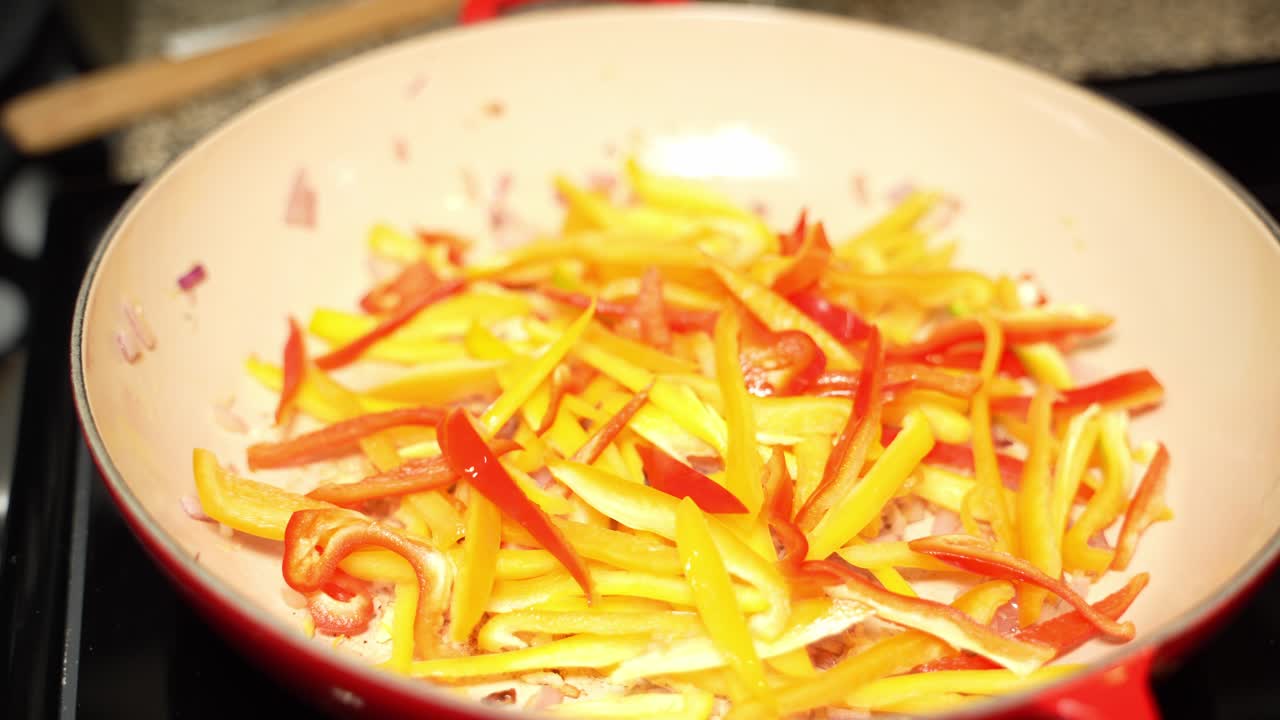 Long slices of orange and red capsicum on frying pan in kitchen.