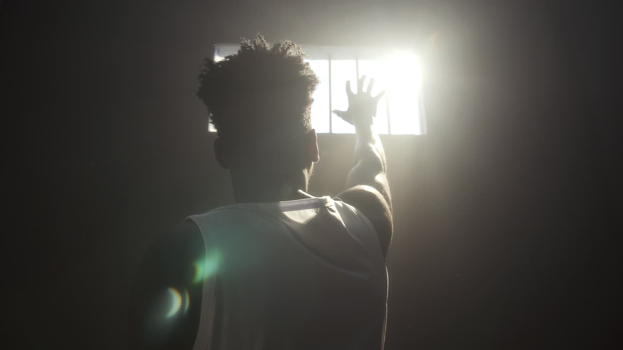 Inmate Reaching toward Bright Sunlight through Barred Window in Prison Cell
