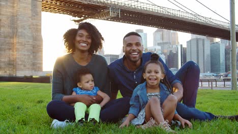 una joven familia negra sentada junto al puente en manhattan, nueva york.