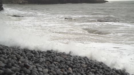 Pan-right-to-left-into-wide-shot-of-Winter-Tide-splashing-in-over-rocky-beach-at-Dunraven-Bay,-South-Wales