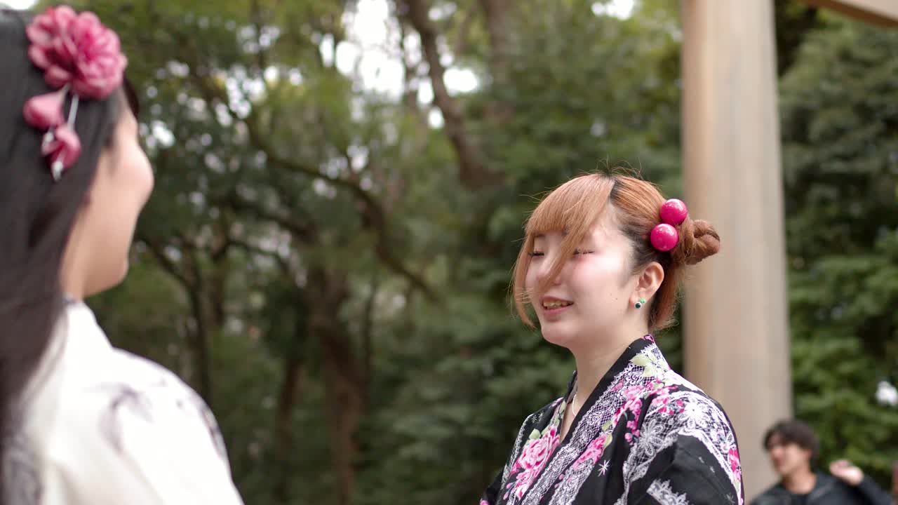 Donne giapponesi in yukata tradizionali si inchinano rispettosamente vicino a un torii in un santuario boscoso.