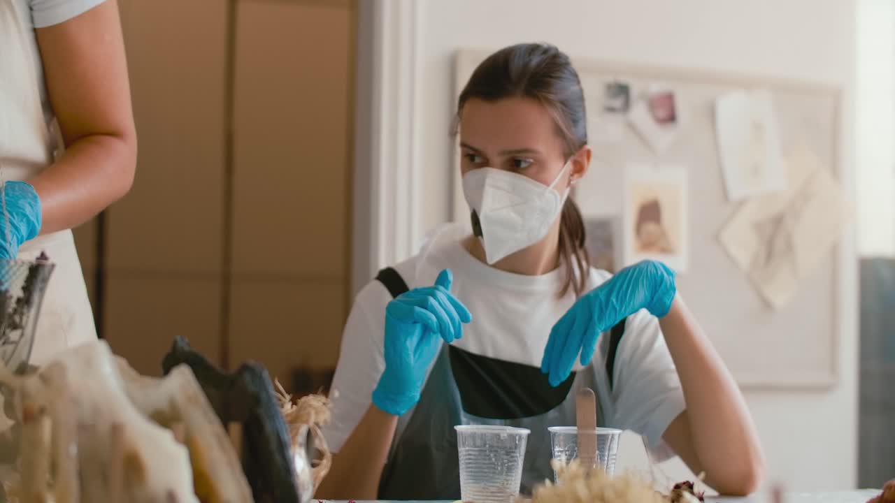 Two women learn a craft in a workshop wearing face masks and gloves