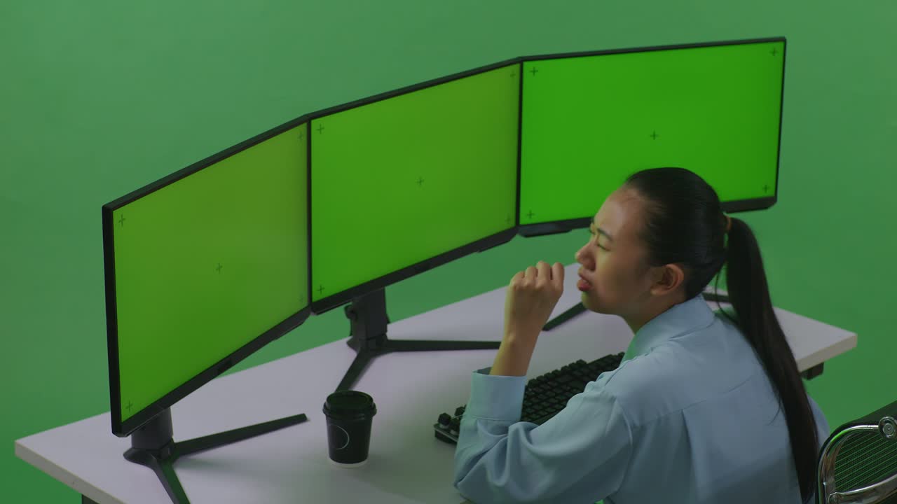 Side View Of Tired Asian Woman Yawning While Working With Mock Up Multiple Computer Monitor In Green Screen Studio