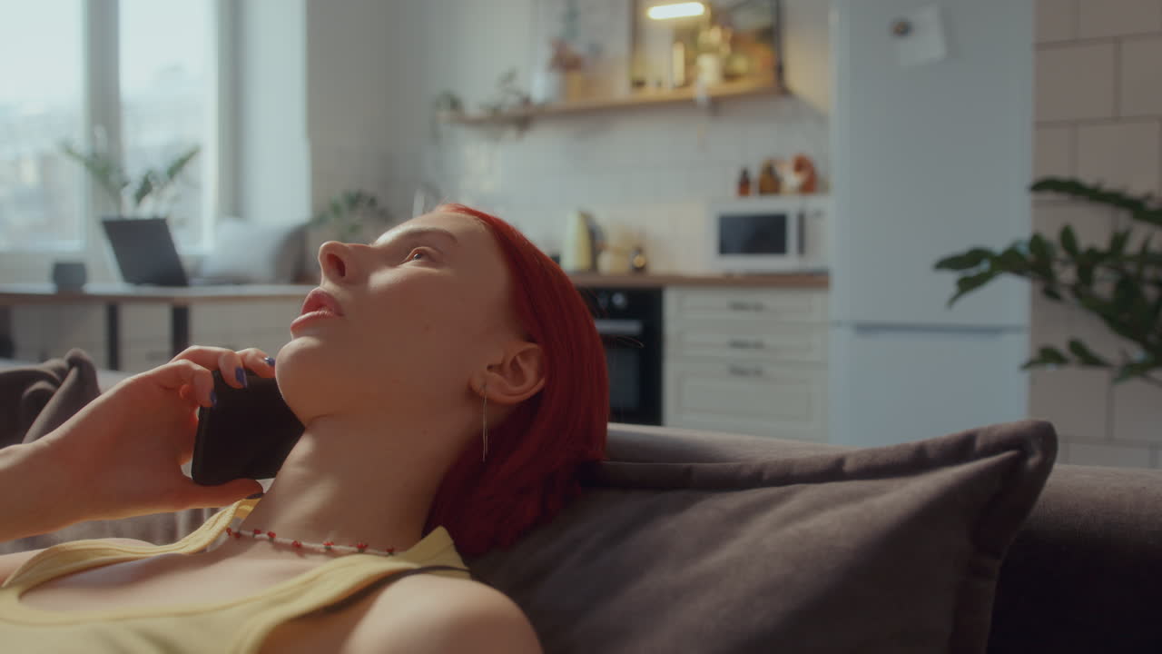 mujer joven descansando en el sofá en casa y hablando por teléfono