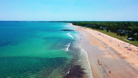 aerial drone video of busy beaches in saco, maine, during peak summer. crowds relax on sandy shores near vacation homes as atlantic ocean waves crash along the lively coastline.