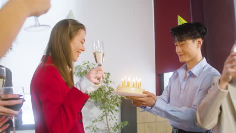 happy woman blowing out candles on cake and drinking with her multiethnic colleagues at the office party