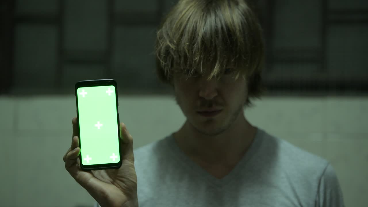 미치광이 무서운 남자가 웃고 초록색 화면으로 전화를 보여줍니다.