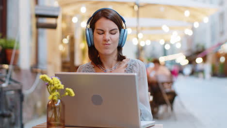 happy young woman in wireless headphones choosing, listening music dancing outdoors city restaurant