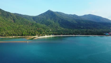 Peaceful-blue-turquoise-lagoon-bordered-by-white-sandy-beach-on-tropical-island-with-green-rainforest-on-hills,-Thailand