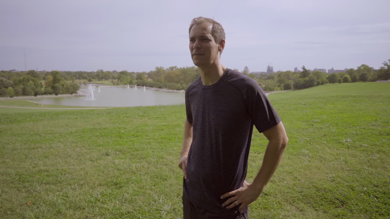 공원에 있는 남자는 달리기 후 언덕 꼭대기에 서서 수평선을 응시한다