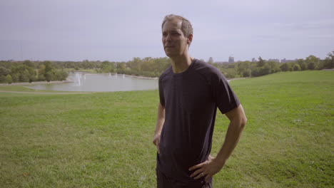 Man-in-the-park-stands-at-top-of-hill-after-a-run-and-gazes-off-to-horizon