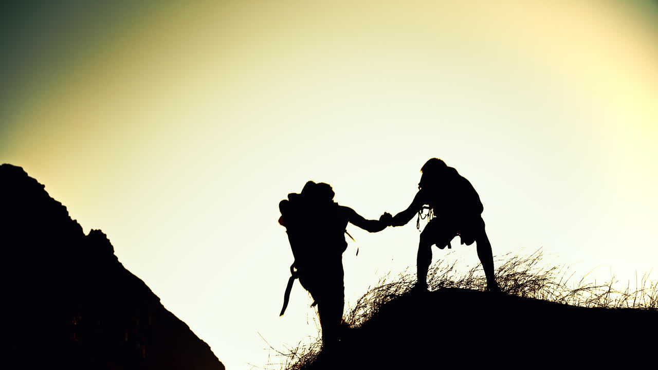 Silhouettes of Hikers Helping Each Other Climb a Hill at Sunset
