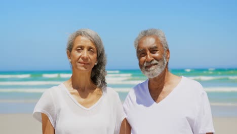 Front-view-of-active-senior-African-American-couple-with-arms-around-standing-on-the-beach-4k