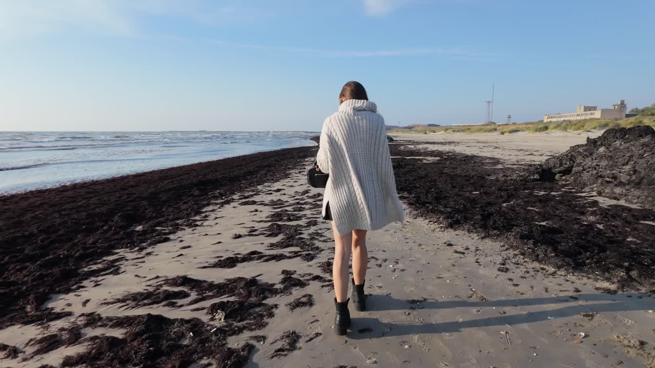 Slow motion of woman walking near seaweed on beach showing environment loss