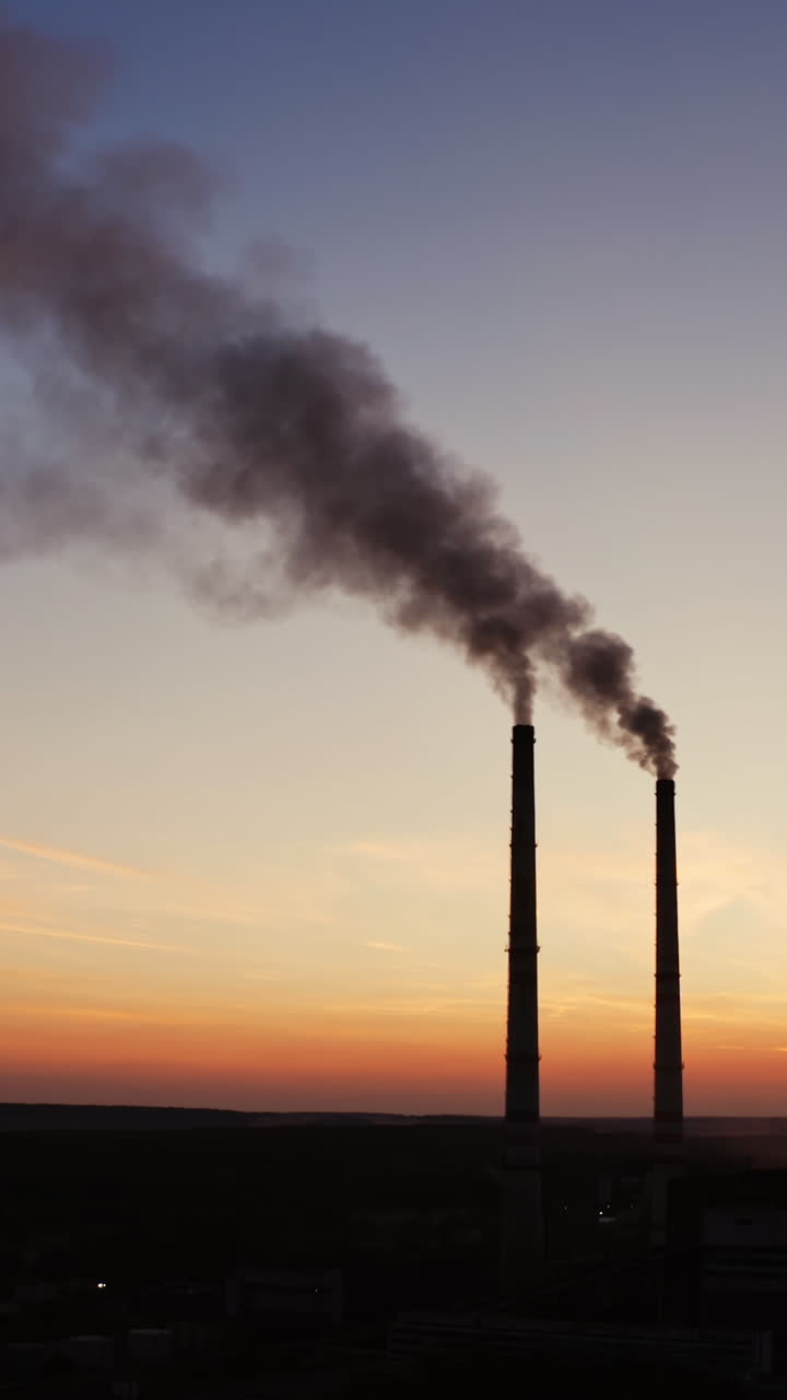 Dirty smoke from industrial pipes over the clear evening sky. Chemical smoke comes out of the pipes of power plant at darkness. Vertical video