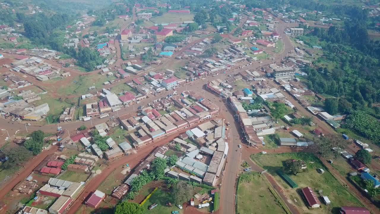 Drone pulls away revealing Kapchorwa town in Eastern Uganda with its clustered buildings, busy roads, and surrounding green highlands from a high aerial vantage point
