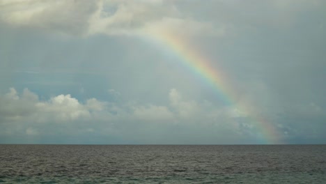 Refracted-sunlight-from-raindrops-creating-colorful-arc-above-the-ocean-surface