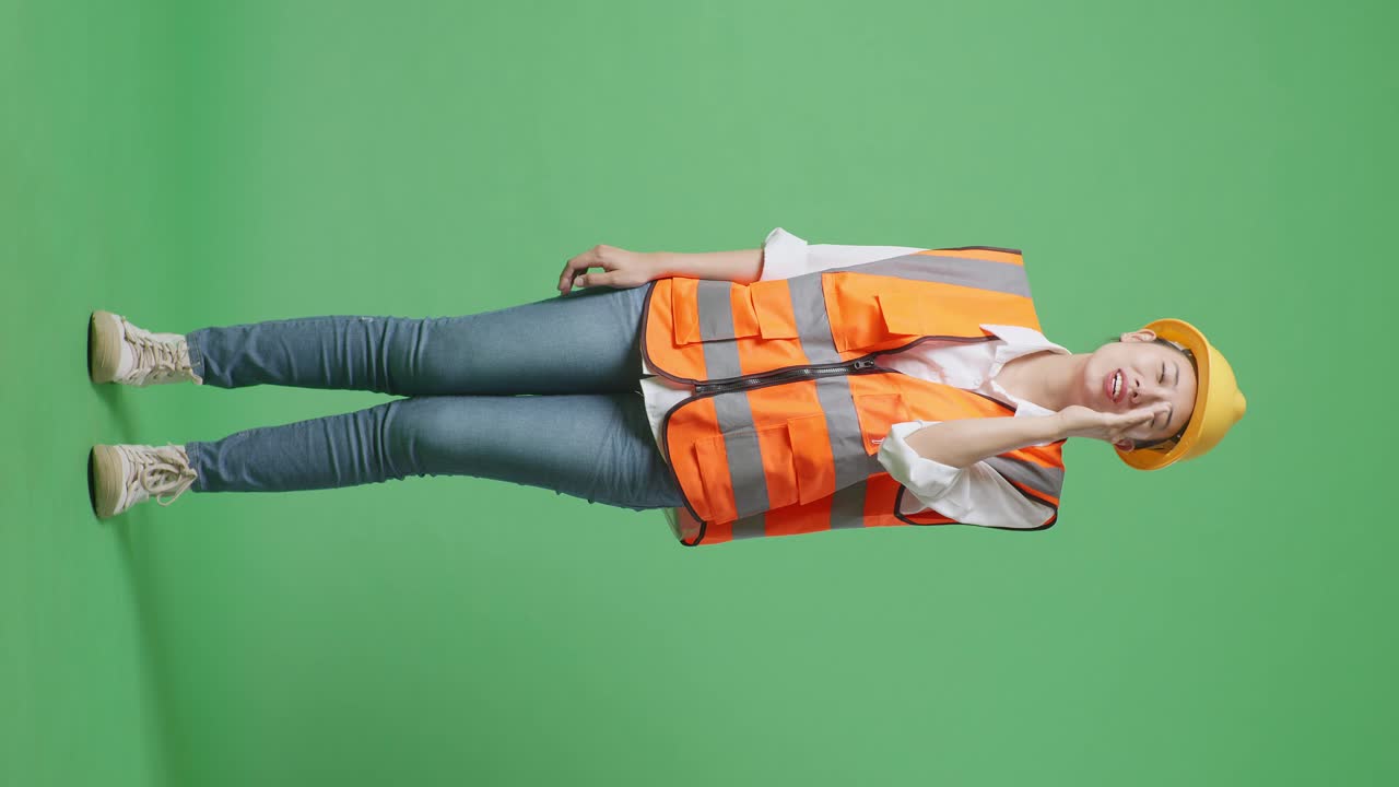 안전 헬을 입은 아시아 여성 엔지니어의 몸이 가득 차 있으며, 녹색 스크린 배경 스튜디오에 서있는 동안 입 위에 손으로 소리치고 있습니다.