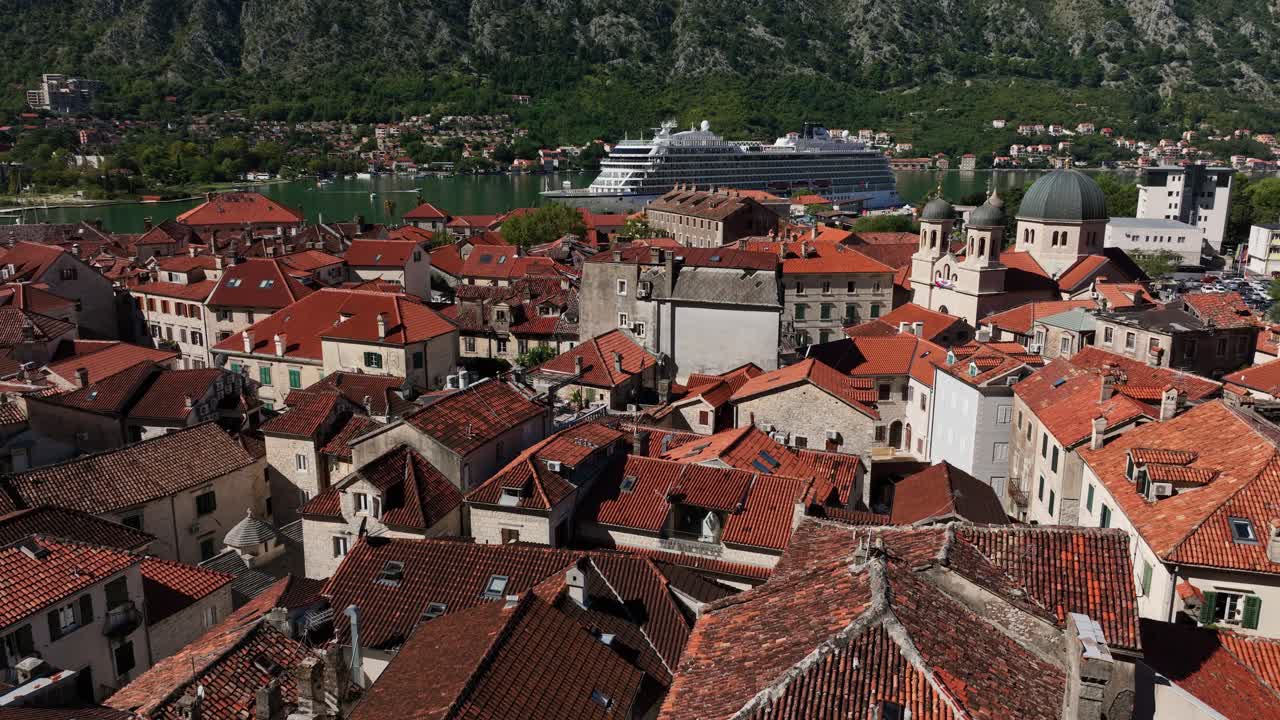 Pan drone shot of big white boat on the Adriatic Sea and cityscape of Kotor during the day in Montenegro
