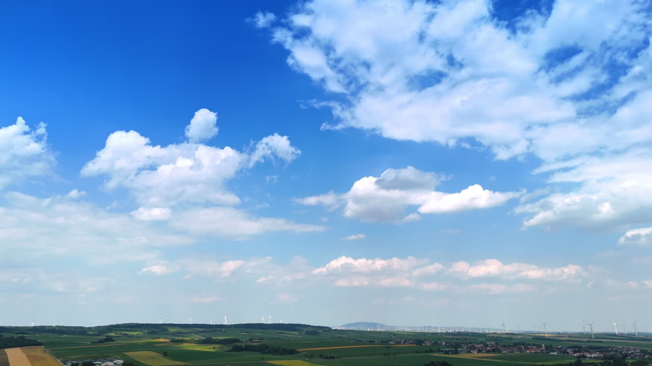 Beautiful blue sky with white clouds over the fields. Numerous wind mills can be seen at backdrop. Aerial view