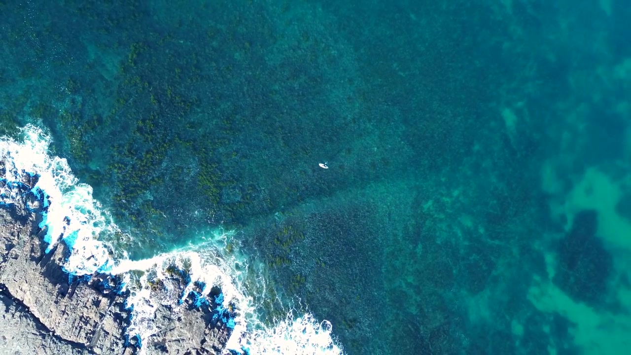 Paesaggio aereo con drone di un solitario praticante di stand up paddle che rema vicino alle onde dell'oceano che si infrangono su una baia rocciosa con isola corallina vicino a Wollongong, sulla costa meridionale del NSW Australia, turismo e tempo libero