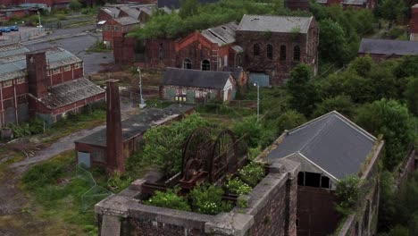 abandoned old overgrown coal shaft rusting wheel industrial museum buildings aerial rising view