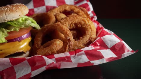 red and blue light reflect off black table top with basket cheeseburger and onion rings, slider 4k