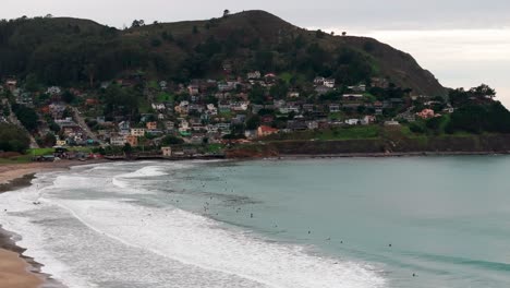 un drone de amplio ángulo volando hacia cientos de surfistas surfeando las olas.