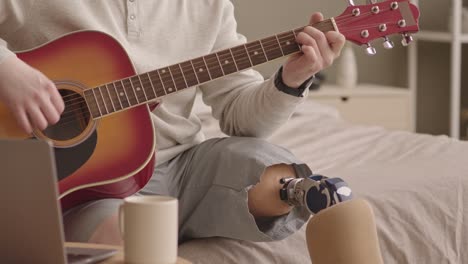 man with prosthetic leg playing guitar at home