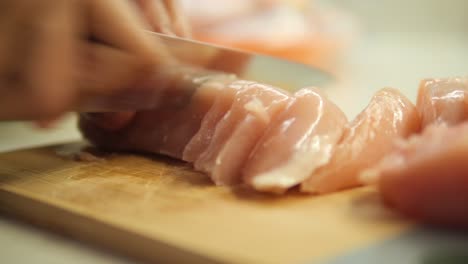 close-up of a knife cutting a chicken breast into thin strips on a wooden cutting board