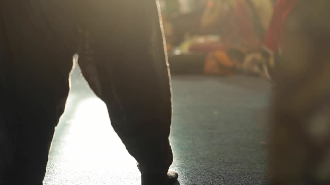 Hindu celebration and people are dancing. Feet are in shot. One lady in semitransparent dark blue trousers dancing side to side. Sun rays are shining towards camera. Filmed in HD