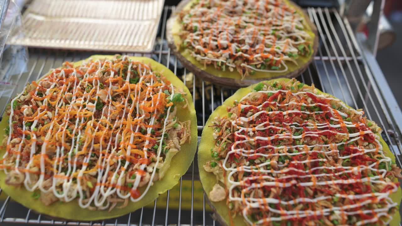 Grillet rispapir med revne gulerødder serveret fra en gadebod. Nærbillede af vietnamesisk gadesælger, der tilbyder sprøde rispapirssnacks toppet med mayonnaise og urter