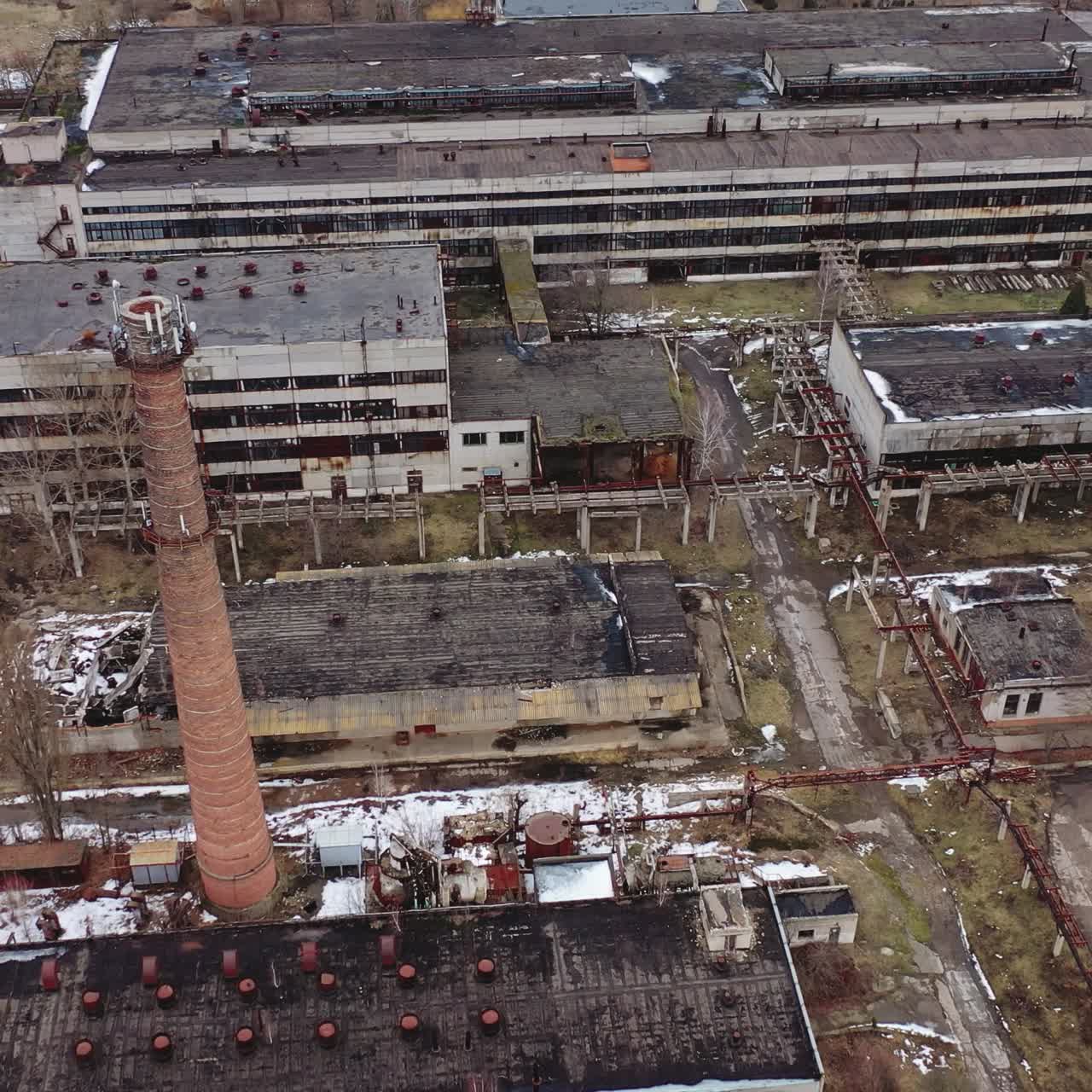Abandoned industrial edifices for demolition. Ruined production buildings with an old brick pipe on the factory territory. Aerial view