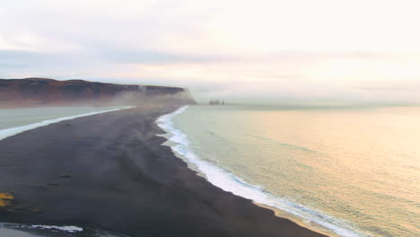 aerial cinematic drone fly path over ocean stunning sunrise early winter at black sand beach apostles fire and ice ocean next to dyhrolaey lighthouse reynisfjara iceland