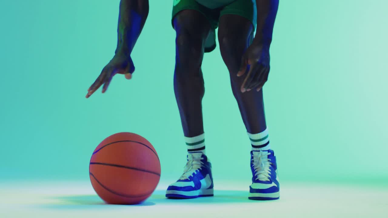 Video de la parte inferior del cuerpo de un baloncestista afroamericano masculino botando un balón sobre un fondo azul