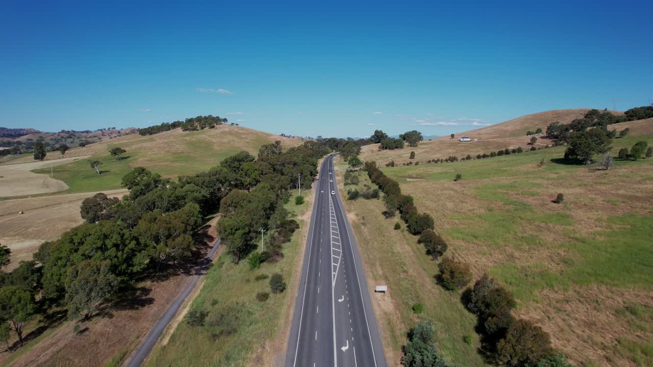 coches circulando por una carretera rural recta con verdes colinas ondulantes, antena