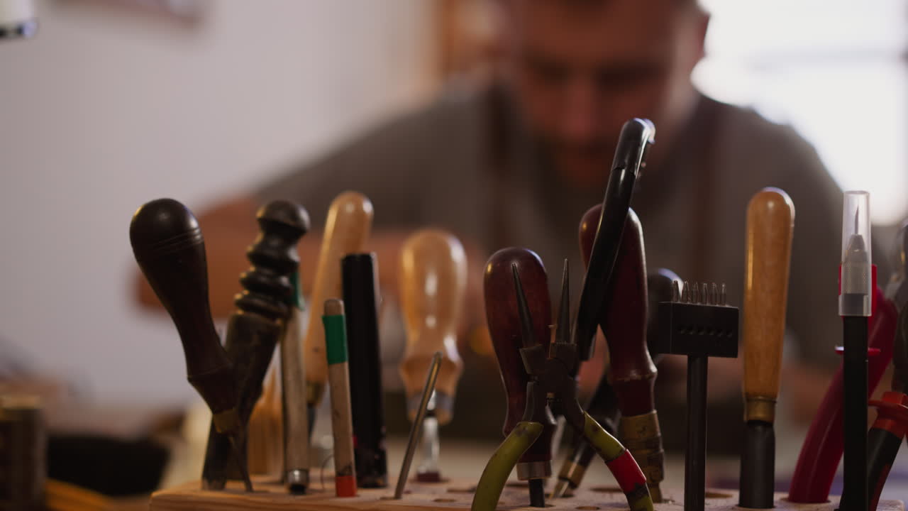 Worker takes cutter for leather from wooden rack in workshop