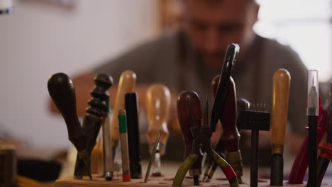 worker takes cutter for leather from wooden rack in workshop